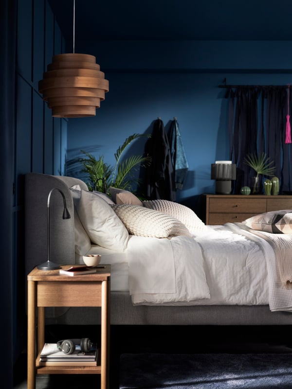 A TUFJORD upholstered bed covered in an OFELIA VASS 3 comforter in a blue room with a DYKARKLOCKA pendant lampshade above it.