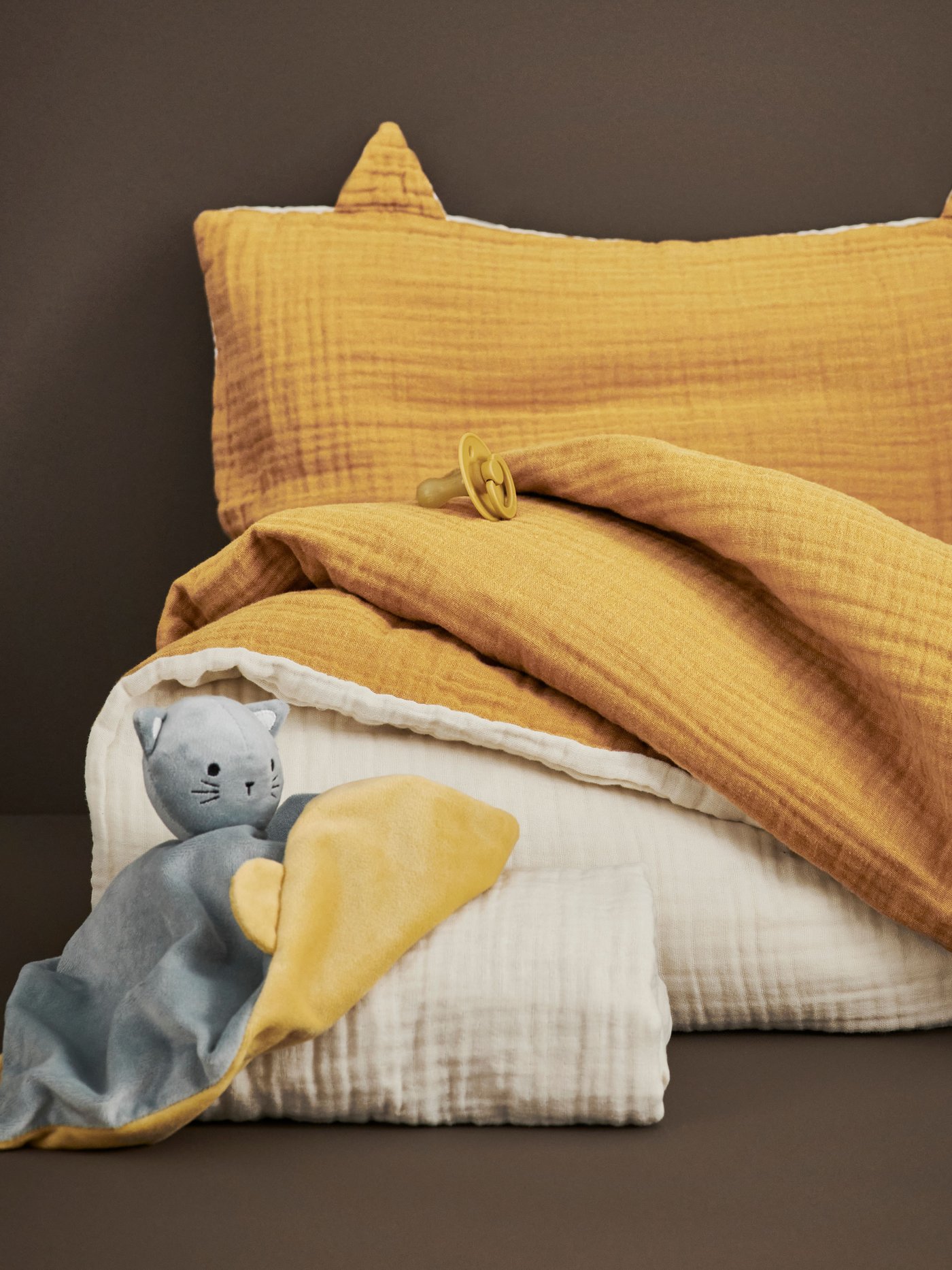 Lähikuva tummankeltaisesta GULDVÄVARE-vuodevaatesetistä ja GULDVÄVARE unihuovasta/pehmolelusta.