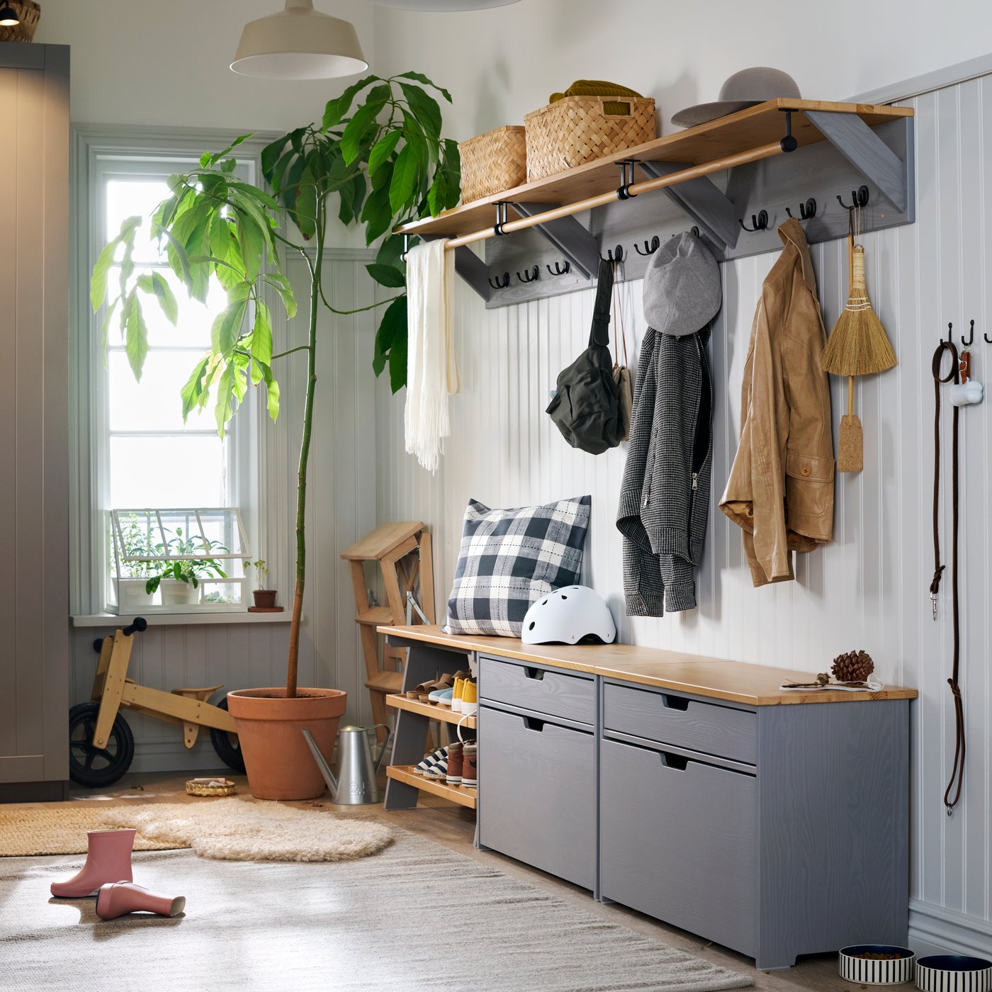 A large and light hallway with a window in the back, white walls and KALLSÖ storage units in grey and wood along right wall.