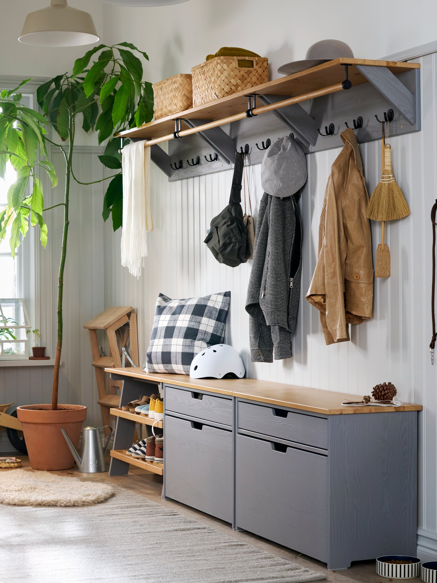A large and light hallway with a window in the back, white walls and KALLSÖ storage units in grey and wood along right wall.