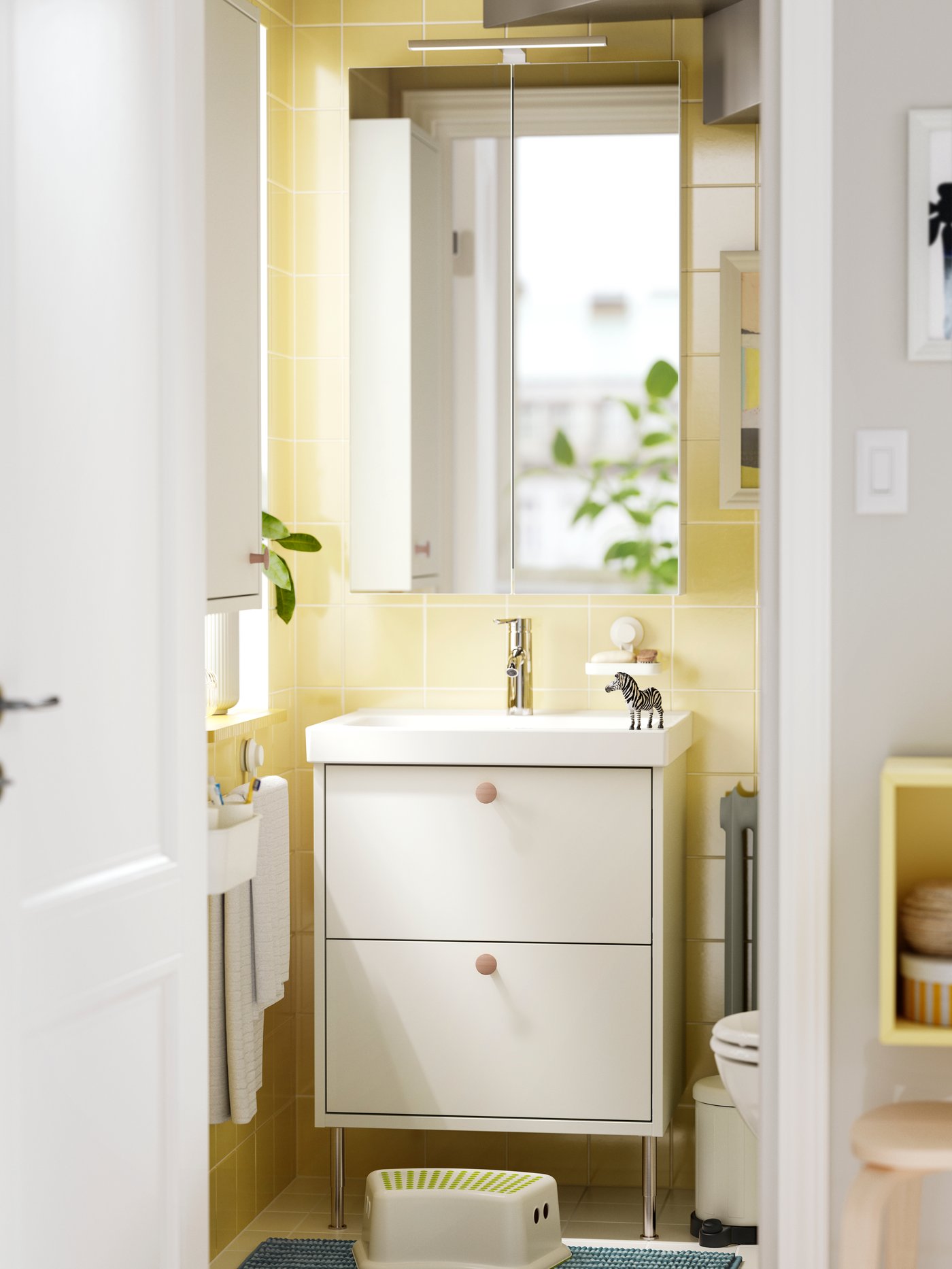 A white HAVBÄCK washstand with drawers and a white HAVBÄCK wall cabinet with a door are mounted in a yellow-tiled bathroom.
