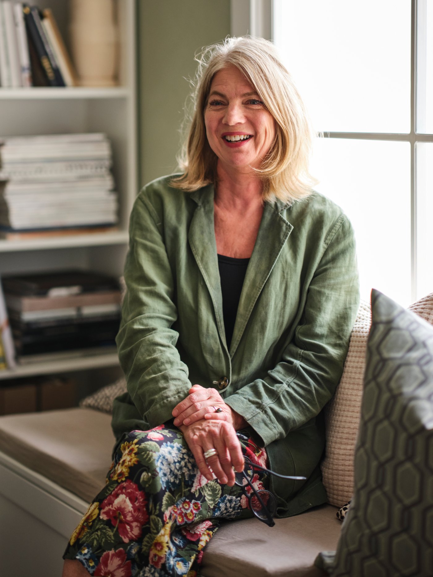 A smiling woman sitting on a white storage bench with scatter cushions in front of a white BILLY bookcase.