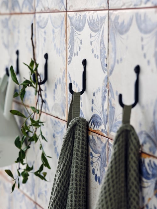 Bathroom area featuring four wall-mounted, black wall hooks, two of which holding flatwoven bath towels.