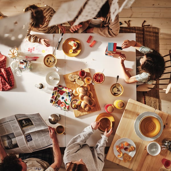 Vue en plongée d’une famille de cinq personnes savourant leur déjeuner autour d’une grande table à manger blanche.