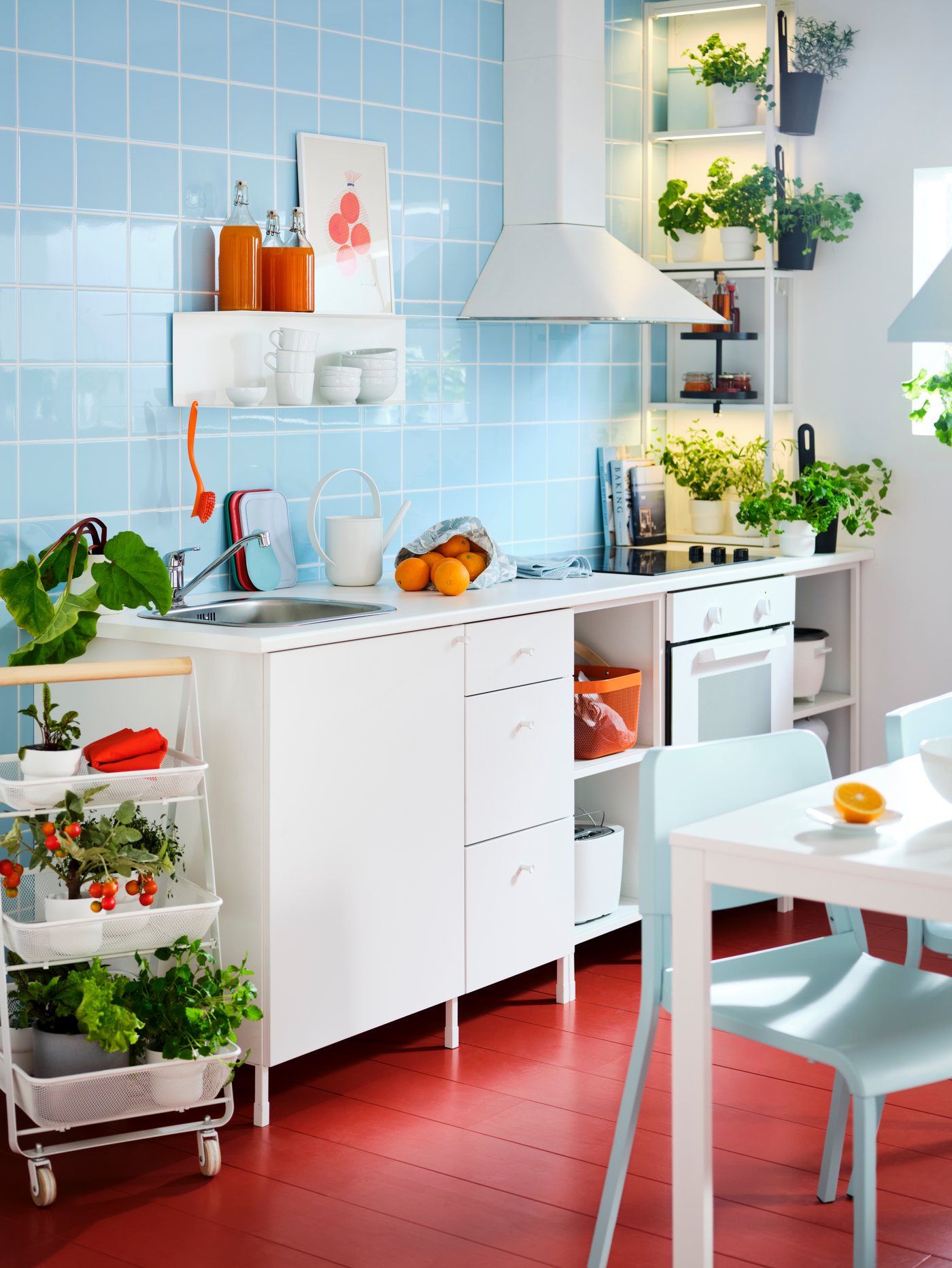 A white ENHET kitchen with wall frames with shelves, a white RISATORP trolley holding herbs and plants and a kitchen table.