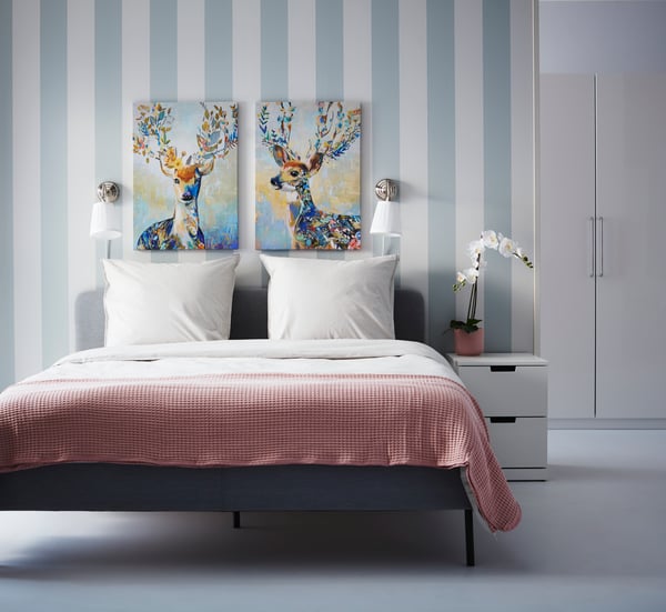 PJÄTTERYD paintings over a bed in a bedroom with blue striped walls.