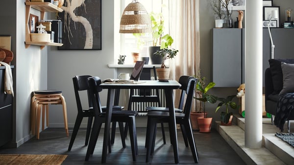 An IKEA LISABO set of four black brown chairs in a Scandinavian style, a matching dining table in front of a sunny window, a rattan lamp shade above, and dark grey flooring.