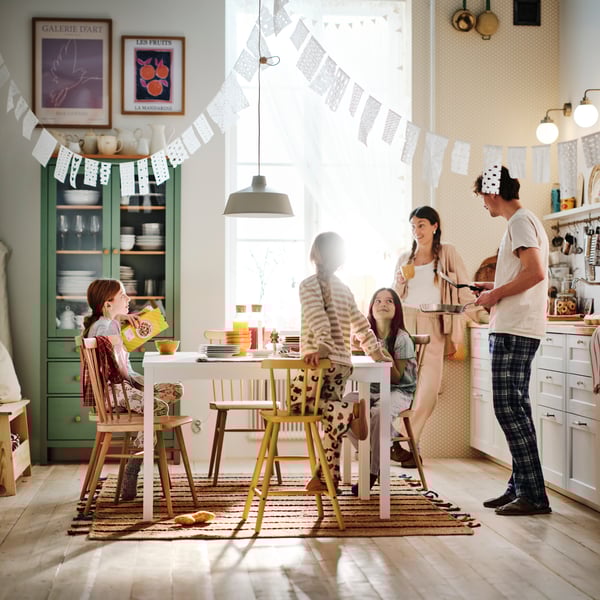 A mum and dad stand in the kitchen looking at the table where their three children are sitting enjoying breakfast.