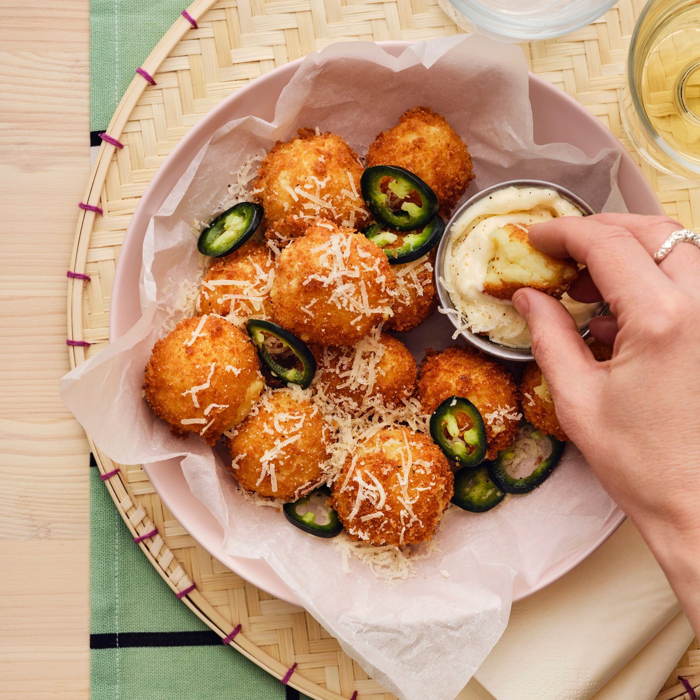 Una mano intinge una crocchetta in una salsa cremosa. Nello stesso piatto, altre crocchette preparate con il purè di patate ALLEMANSRÄTTEN.