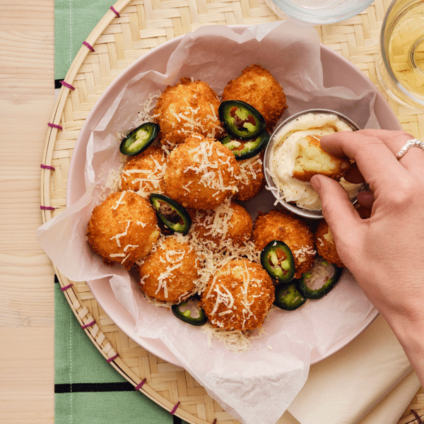 Eine Person taucht eine Krokette aus einer Portion aus ALLEMANSRÄTTEN Kartoffelpüree in eine cremige Soße.