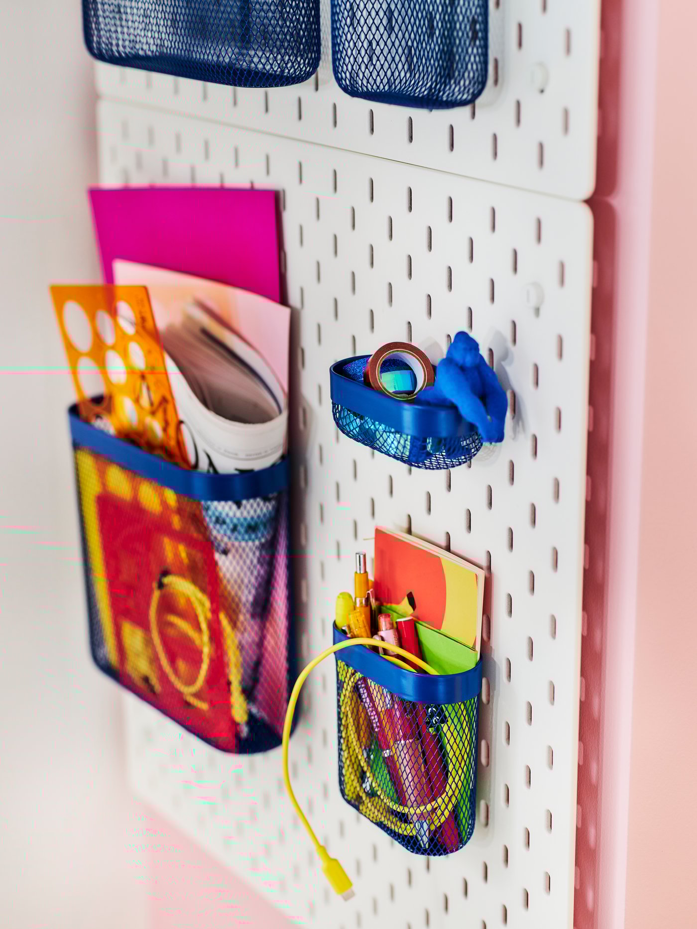 En SKÅDIS opbevaringsplade med blå kurve på, hænger på en lyserrød væg, 