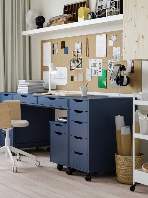 A black-blue ALEX desk in a student room, with on each side a drawer unit. Under the desk sits a smaller drawer unit as too.