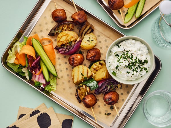 Meatballs on skewers with vegetables and feta dip on the side.