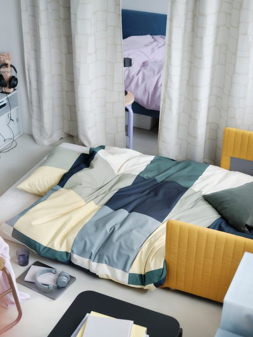 Schlafzimmer mit einem FRIDHULT Bettsofa, das mit blauer BRUNKRISSLA Bettwäsche bezogen ist.