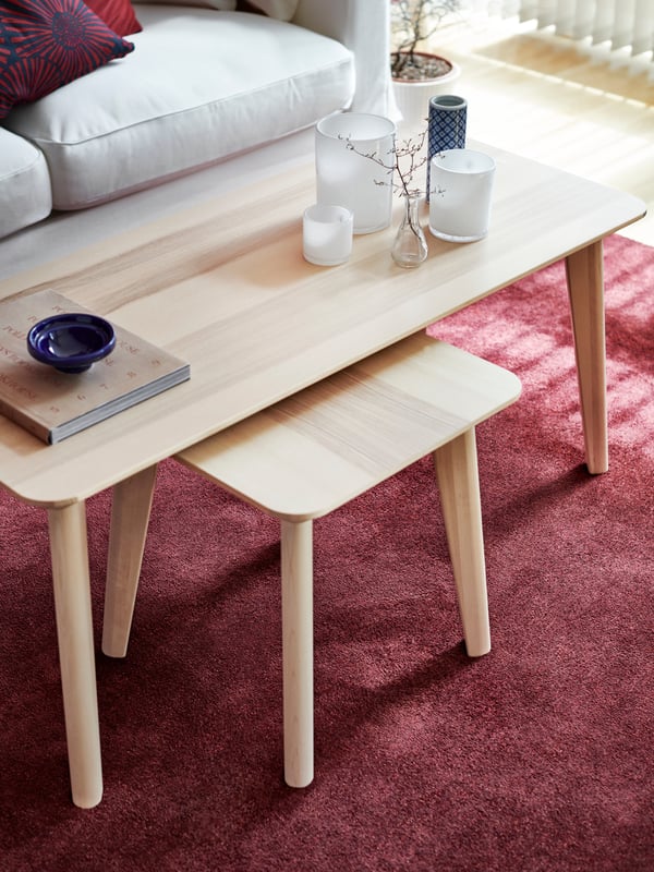 A LISABO table in ash veneer with a wooden stool beneath it, various items on the table and a pink rug under it.