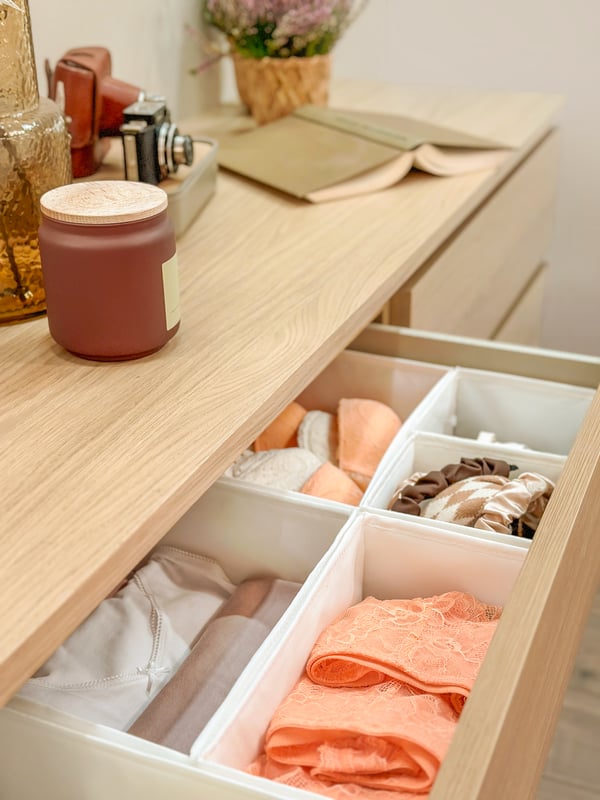 A gray HEMMAFIXARE storage case with clothing in it on the floor partially pulled out from under bed.