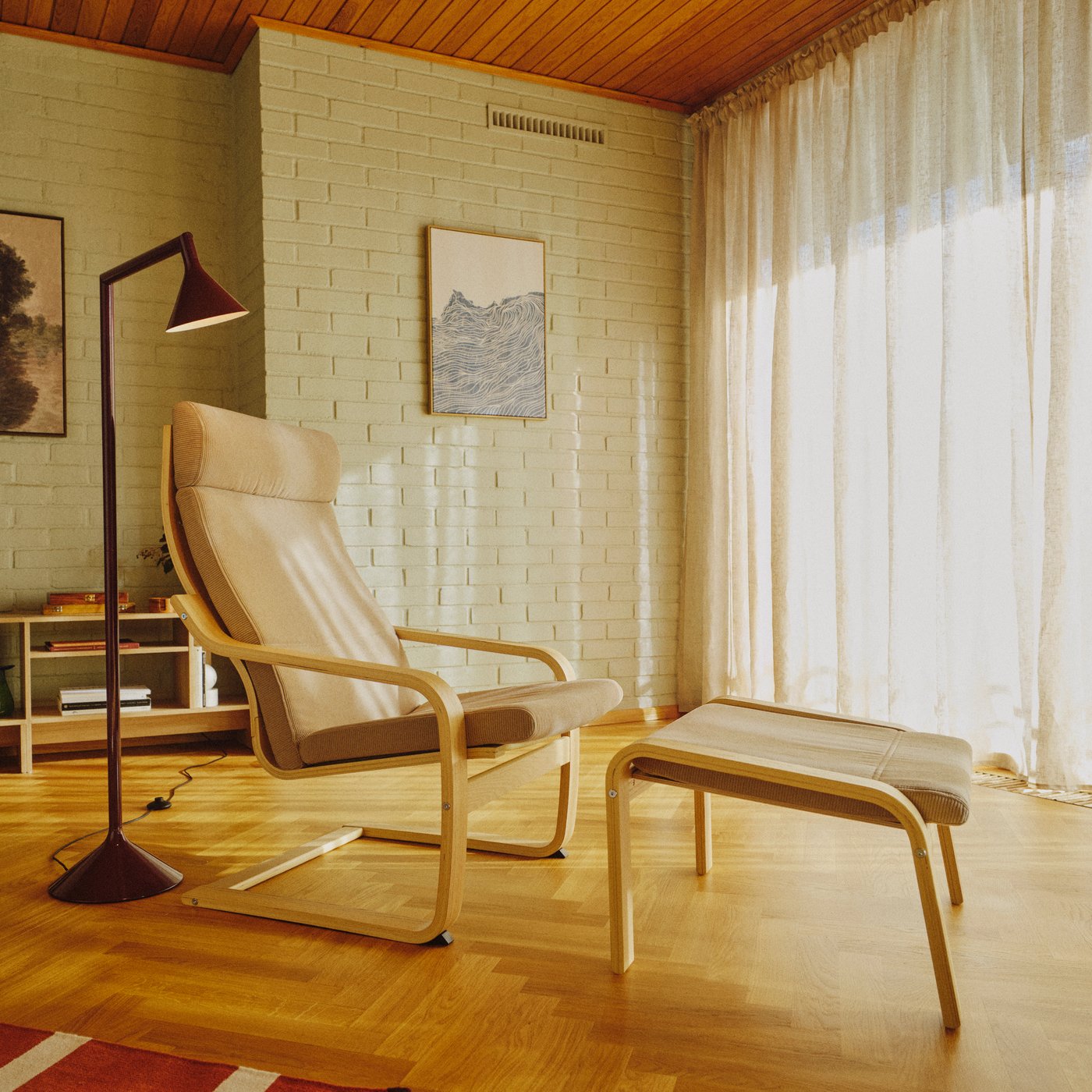 En beige POÄNG lænestol i egetræ med matchende fodskammel står i midten af en varm, minimalistisk stue med trægulv.