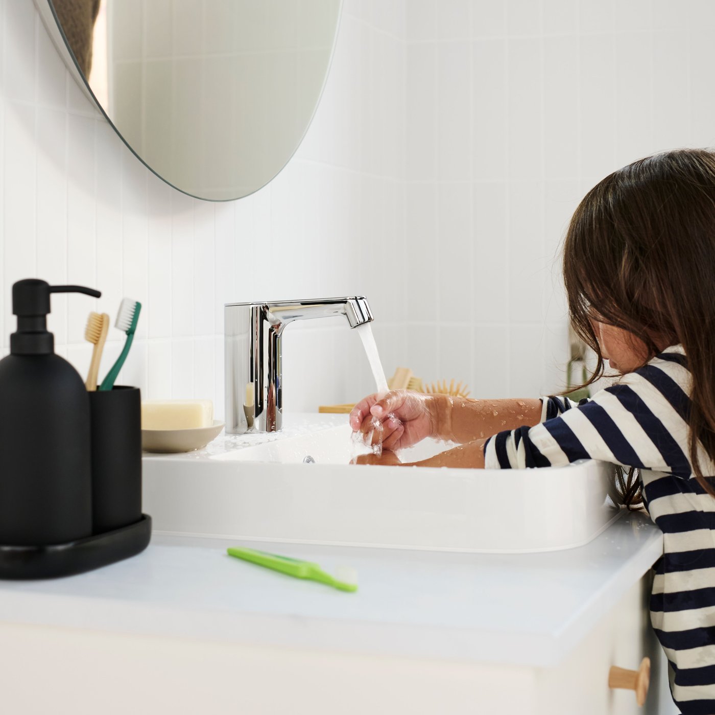 A child is using the BROGRUND wash-basin mixer tap with sensor, with soap and a green brush visible on the counter.
