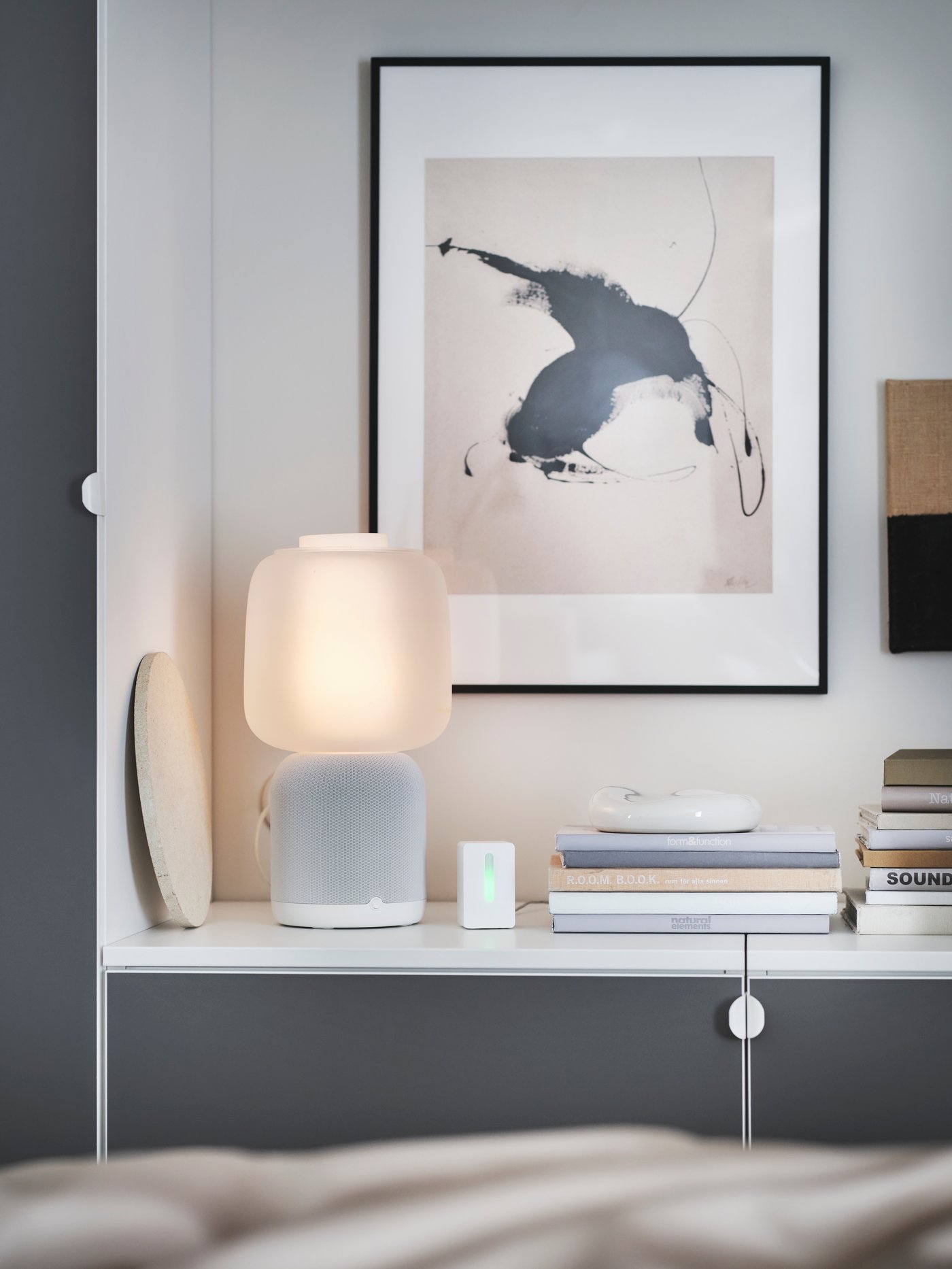 Lampe avec enceinte intégrée posée sur une commode avec un tableau accroché derrière.