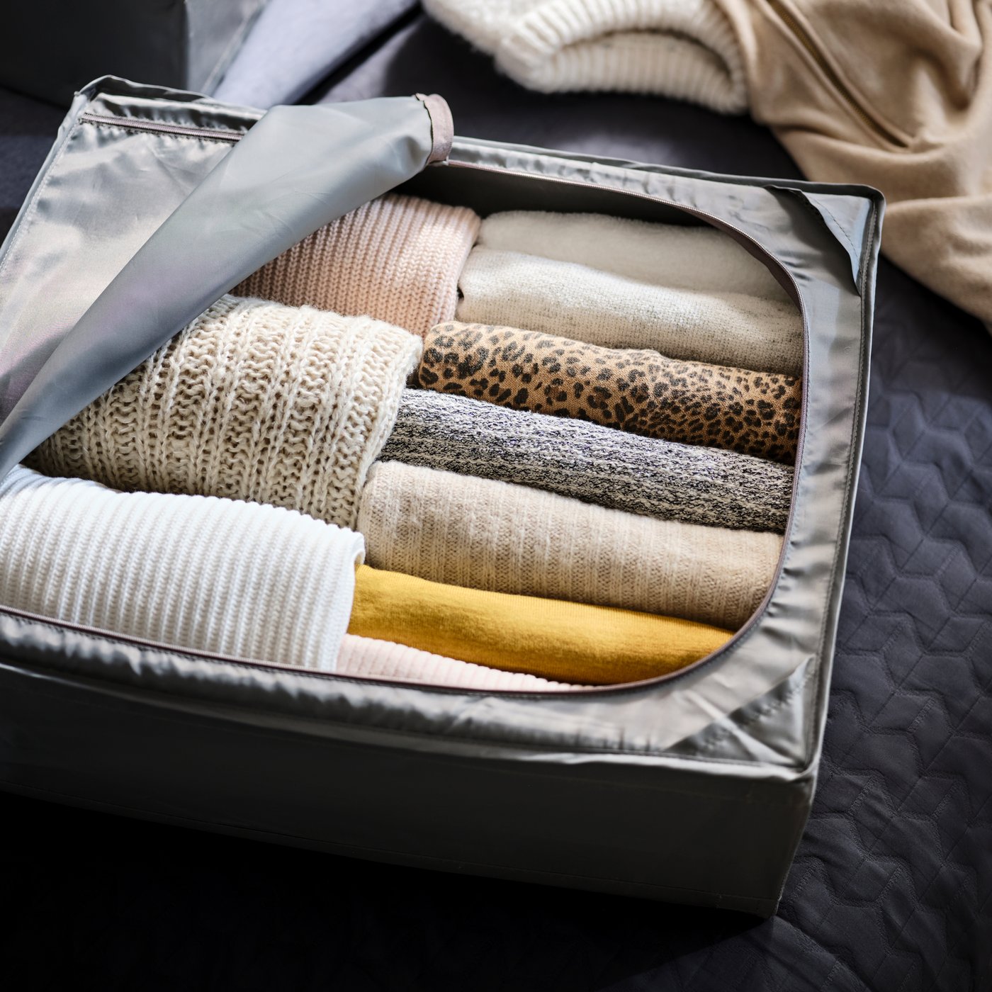 Närbild på en SKUBB grå klädlåda med dragkedja med stickade tröjor innuti. 