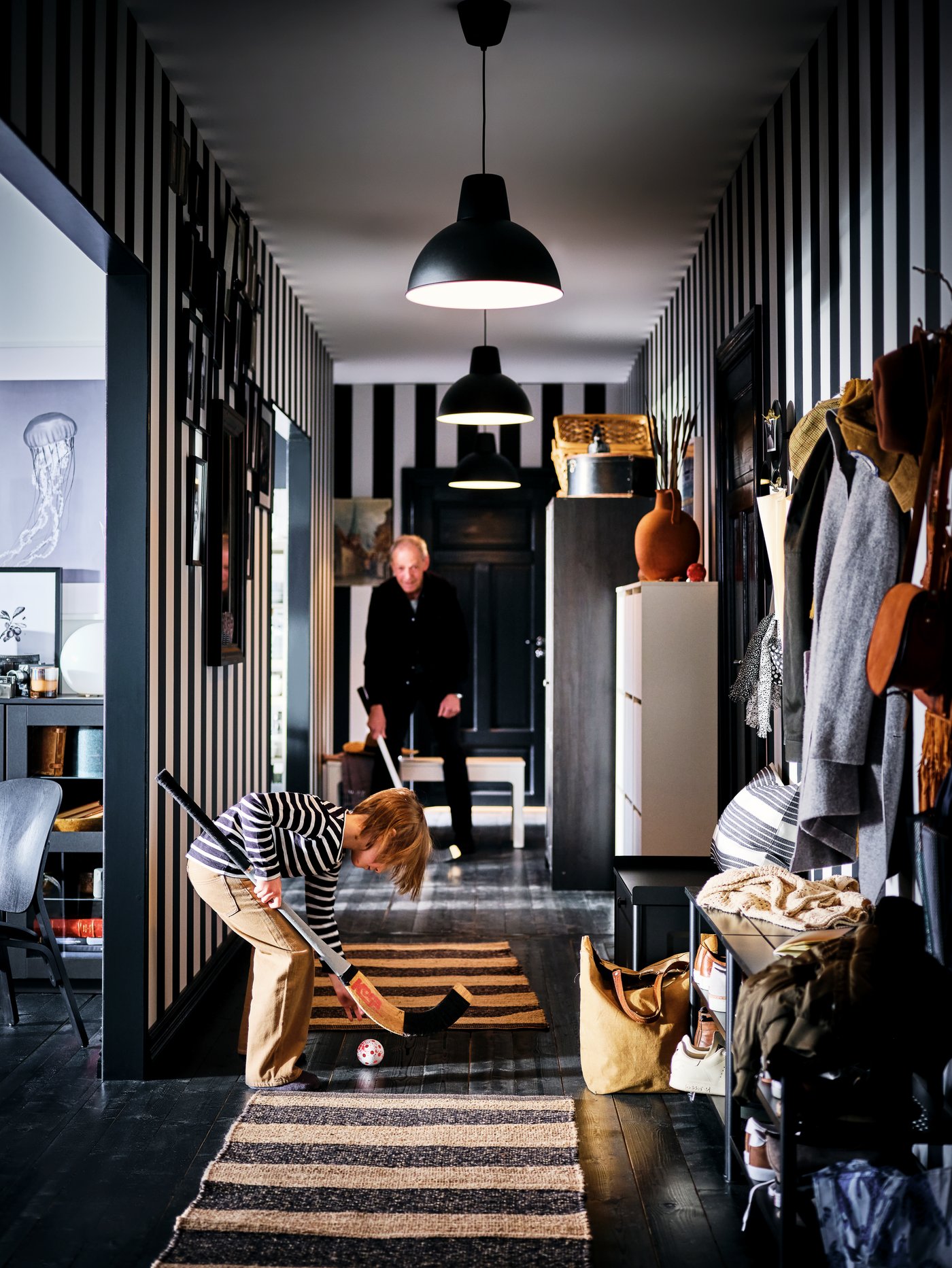 صبي ورجل عجوز يلعبان بمضارب الهوكي والكرة في مدخل طويل ضيق تصطف على جانبيه وحدات تخزين، مثل منصّات PINNIG سوداء.