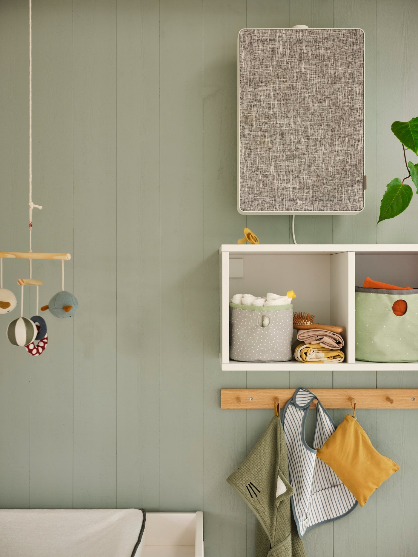 A white FÖRNUFTIG air purifier on a green wall above a shelf with two green/light grey LEN boxes and baby accessories on it.