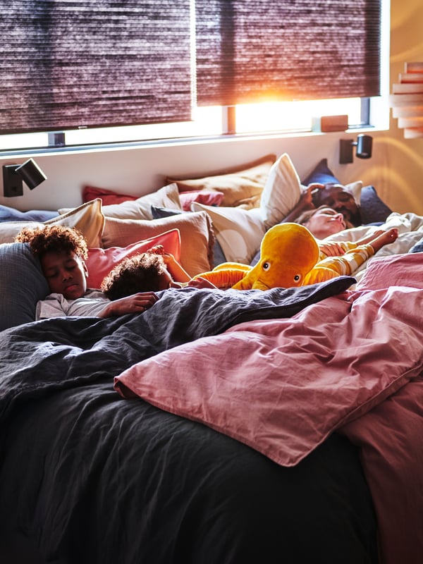 Ein gemütliches Bett mit vielen Decken und einem heruntergelassenem Rollo.