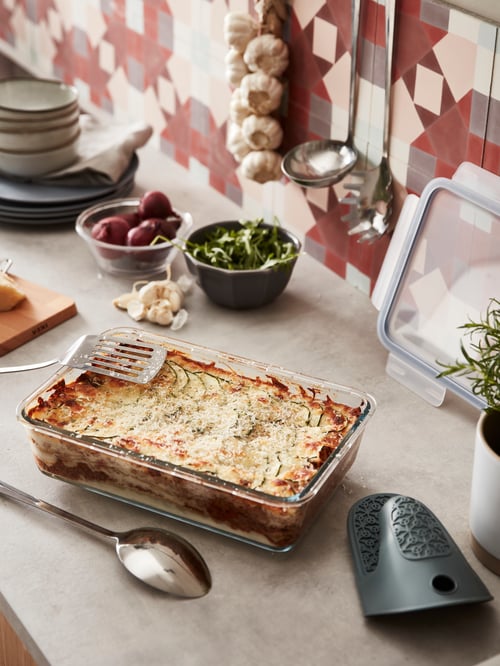 ワークトップに、料理が入ったガラス製IKEA 365+ 食品保存容器。そばに、プラスチック製のふた、キッチン用品、食器。