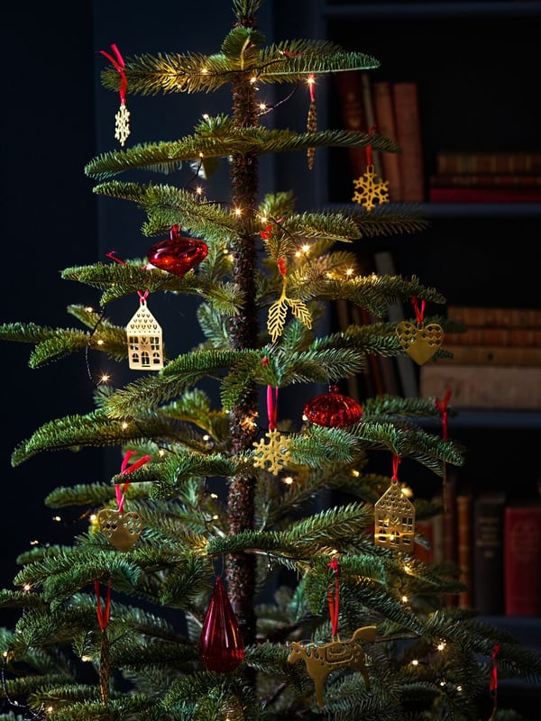 Un albero di Natale artificiale con luci, palline rosse e decorazioni dorate a forma di casetta.