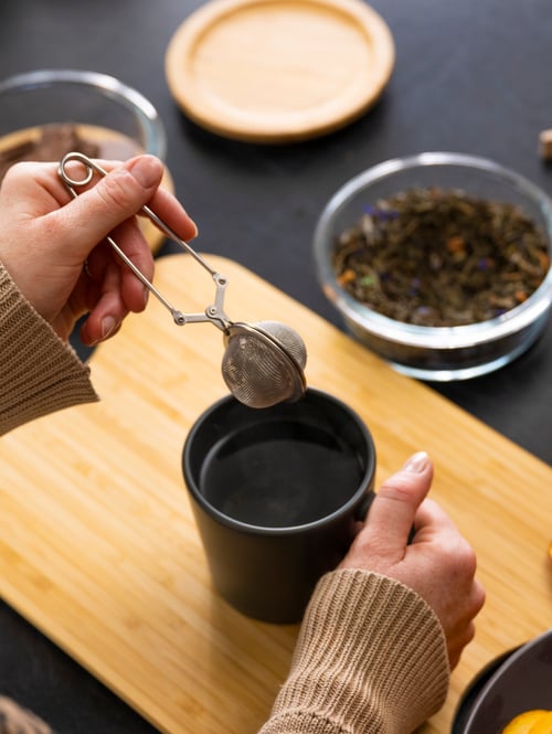 Woman holding an IDEALISK tea infuser above a grey DINERA mug.