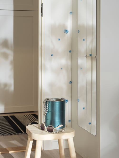 Hallway area with a mirror mounted on a wall to the side, with a green storage bin and a pair of glasses on a stool.