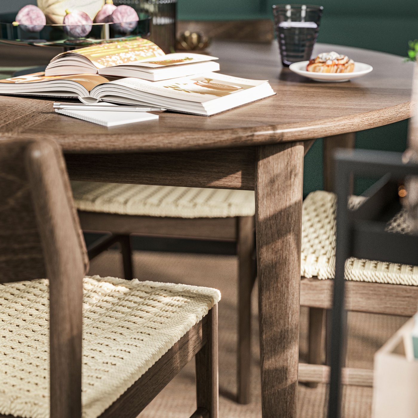 Runt SKANSNÄS träbord med öppna böcker och kaffekopp, omgiven av stolar med flätade sitsar. I bakgrunden syns gröna väggar och dekorativa detaljer.