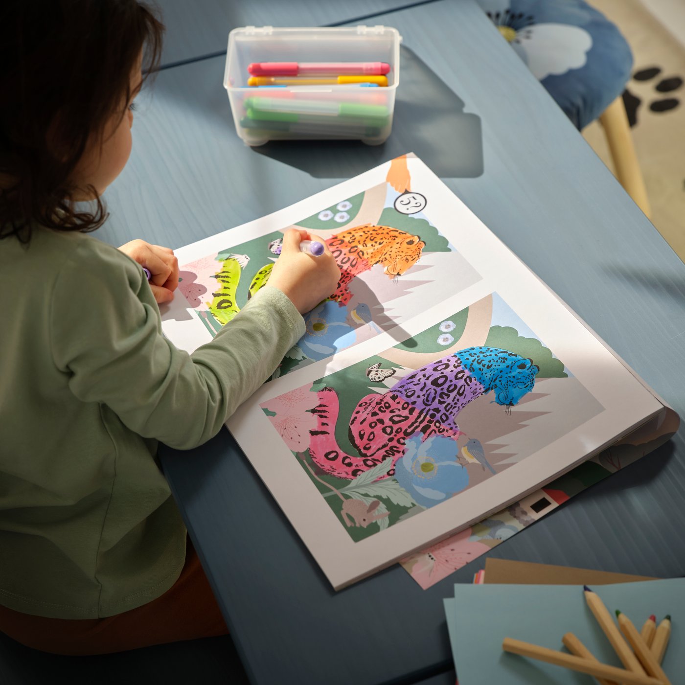 A child colours a leopard in the ALPTALL activity book which has colouring pages and games.