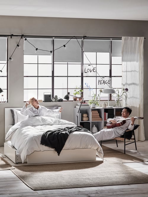 Modern bedroom featuring a bed frame with six spacious drawers, a cabinet, a rug, a pair of curtains, a throw, a reading lamp.