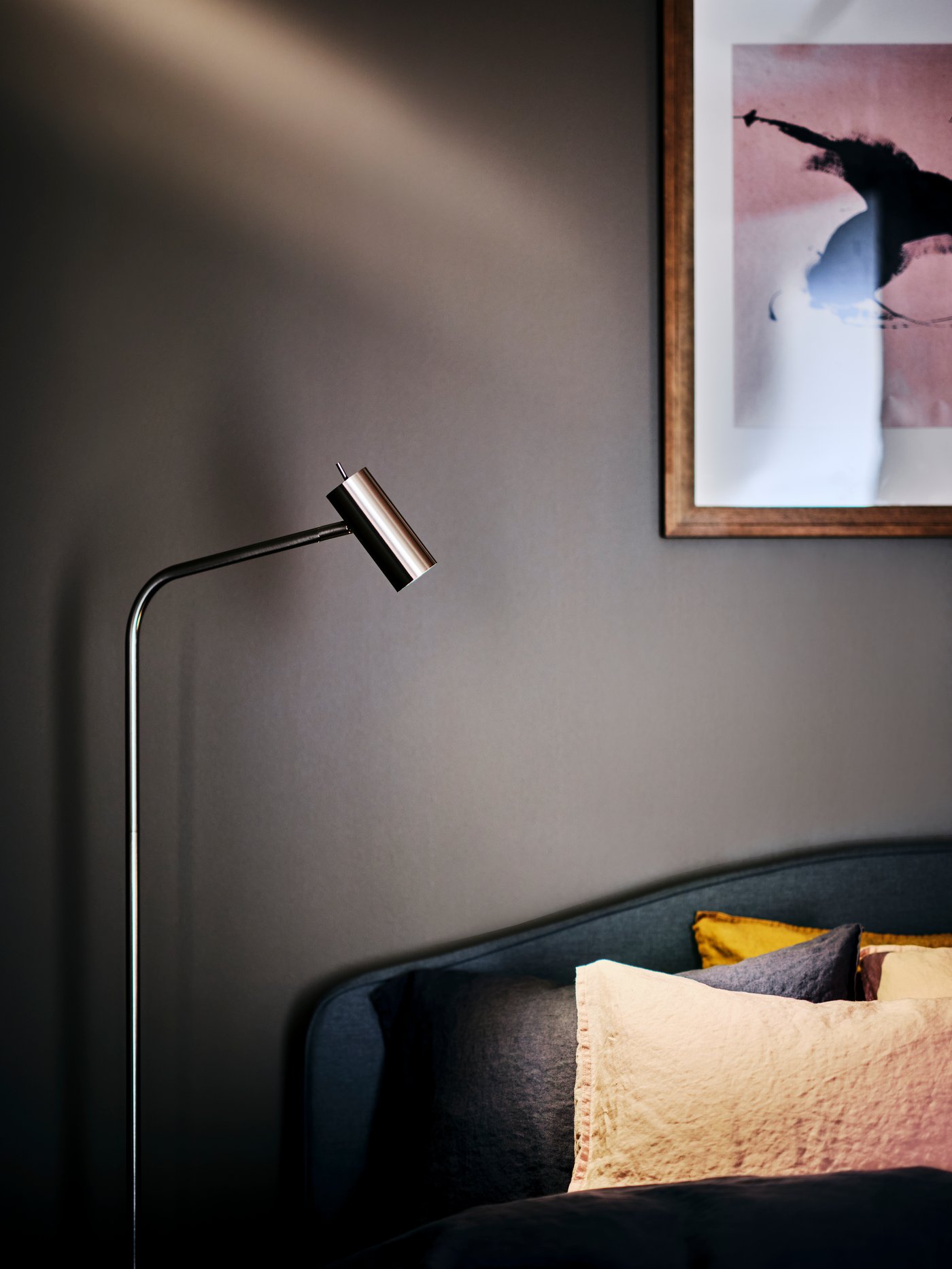 A VIRRMO floor/reading lamp next to a made grey HAUGA upholstered bed with storage.