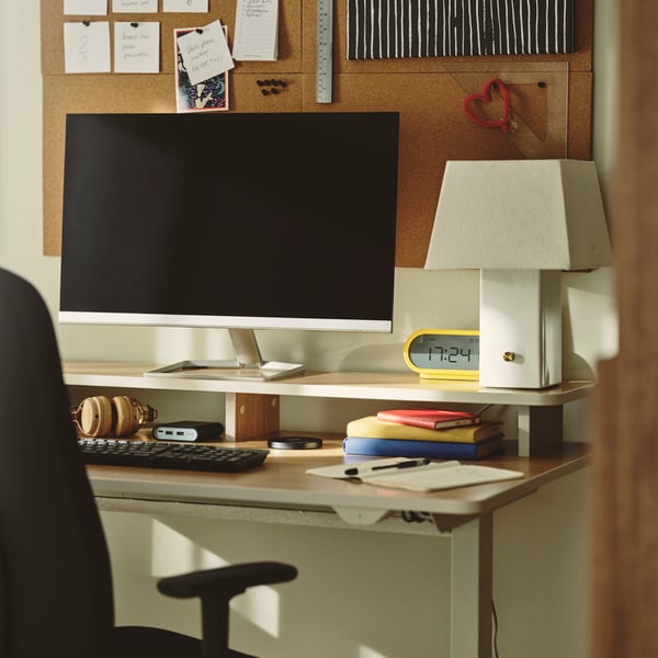 A home office with a beige TRAVSPORT desk sit/stand made from electric oak effect, featuring a computer and stationery.