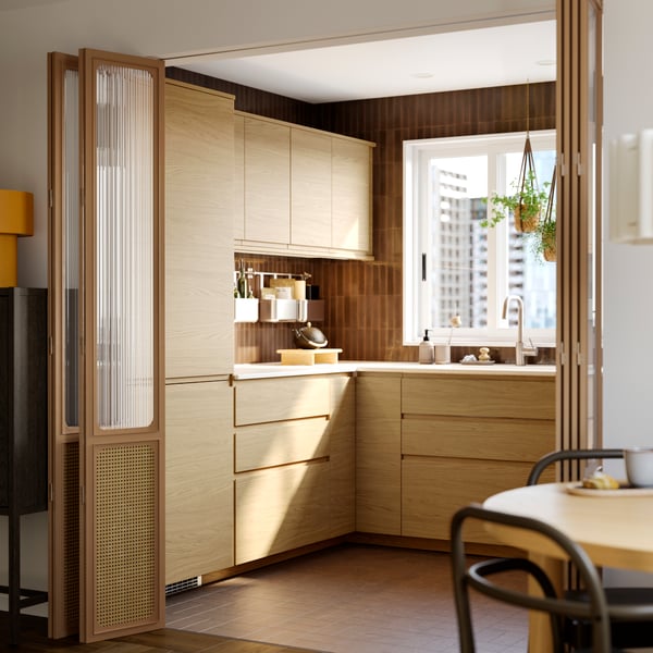 A kitchen with VOXTORP drawers fronts and doors in oak effect, table and chairs, and plants hanging in pots in the window.