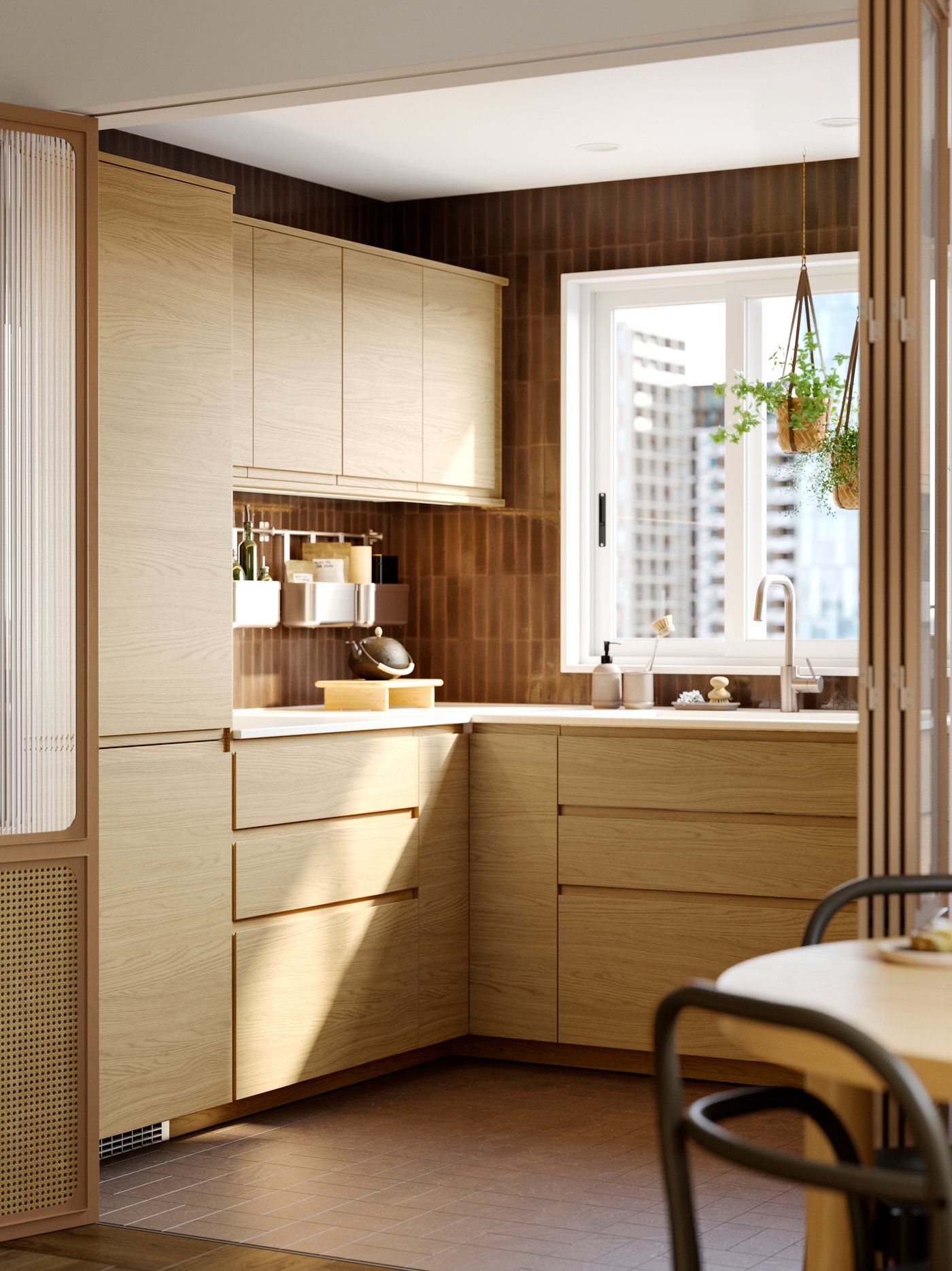 Kuchnia z imitującymi dąb frontami szuflad i drzwiami VOXTORP, stołem i krzesłami oraz roślinami w doniczkach zwisających z sufitu przed oknem.