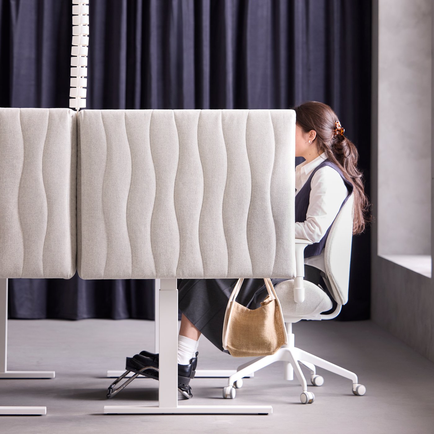 Bureau avec une personne assise à un poste de travail isolé par une cloison acoustique MITTZON Gunnared beige.