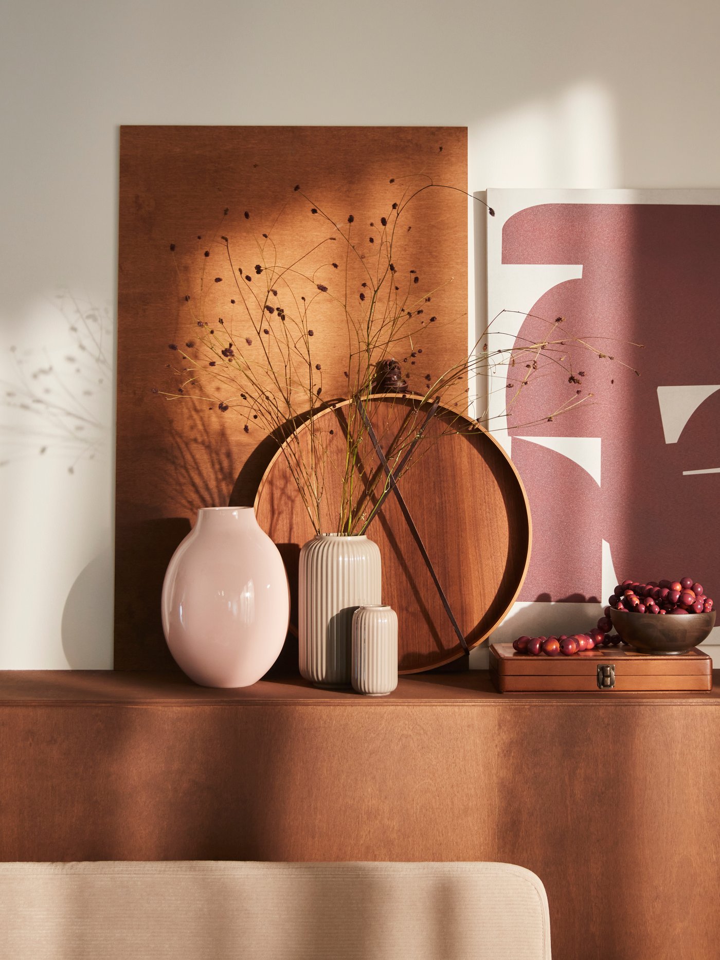 A pale pink BLODBJÖRK vase is placed on a tan surface together with a STILREN vase, decorative objects and a PJÄTTERYD picture.