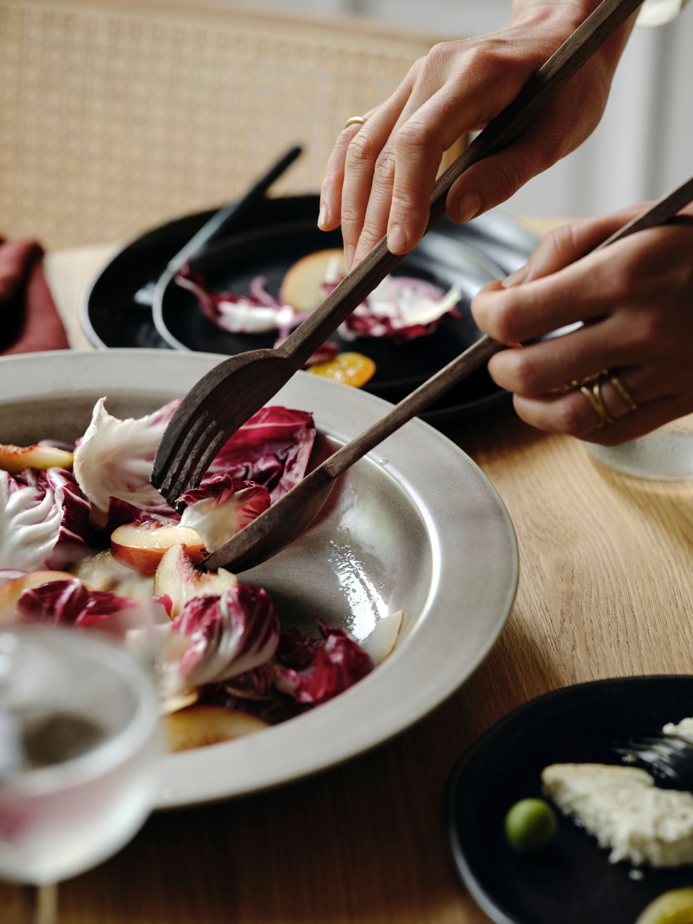 Two hands holding a STOCKHOLM 2025 2-piece serving set in walnut, picking at food in a beige serving bowl.