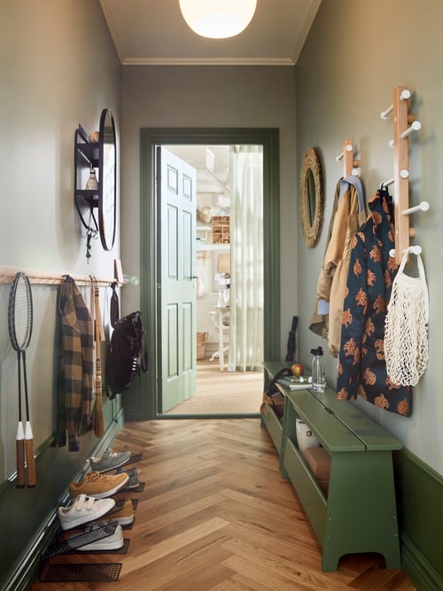 Hallway with a PERJOHAN storage bench, two vertical hook racks with clothes, a mirror with storage, and a rack with clothes.