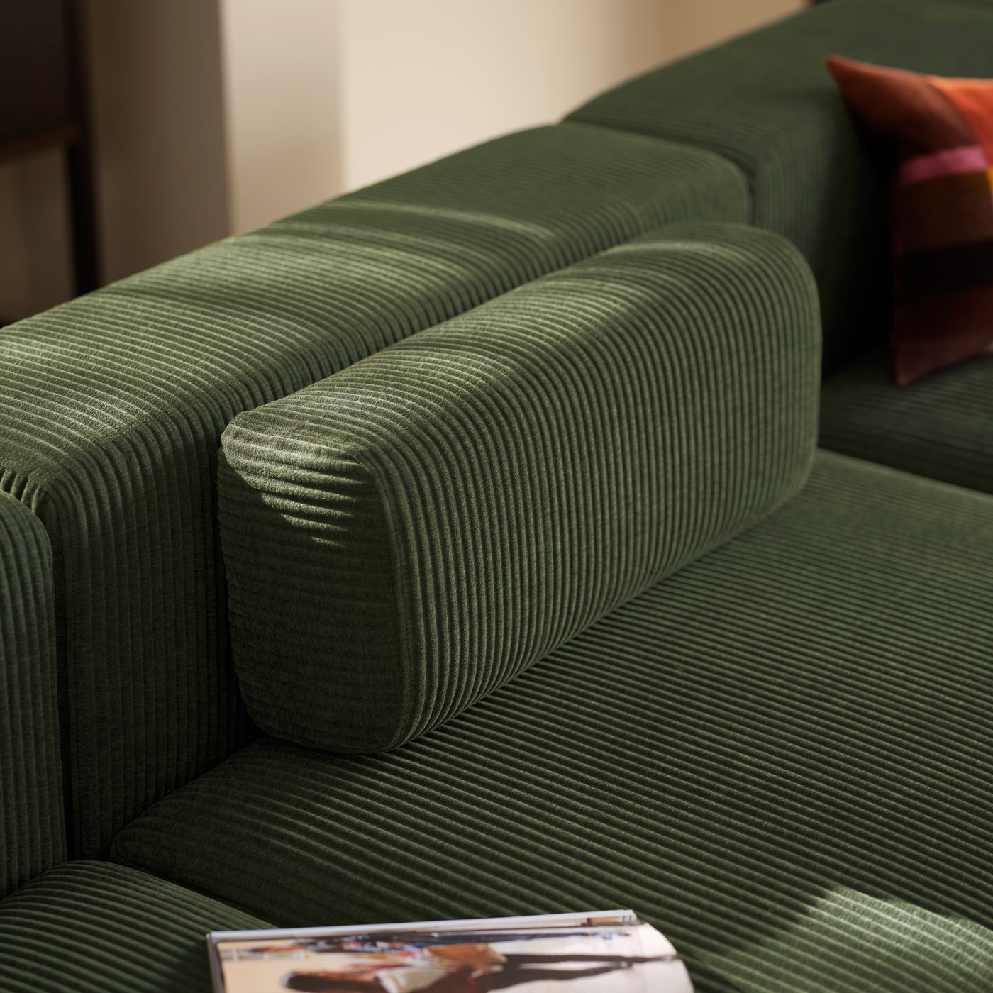 A loose, matching armrest placed by the backrest of a dark-green JÄTTEBO four-seat sofa, flanked by a cushion and a magazine.