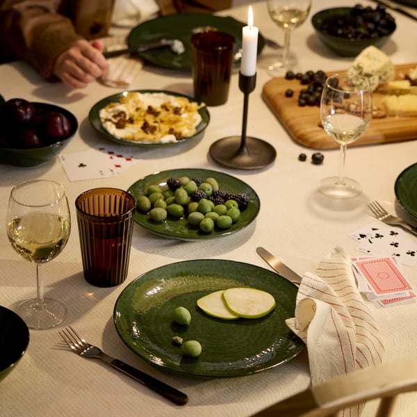 People are gathered around a dinner table for a meal of cheese and fresh fruit, all in a cosy, atmosphere with candles.