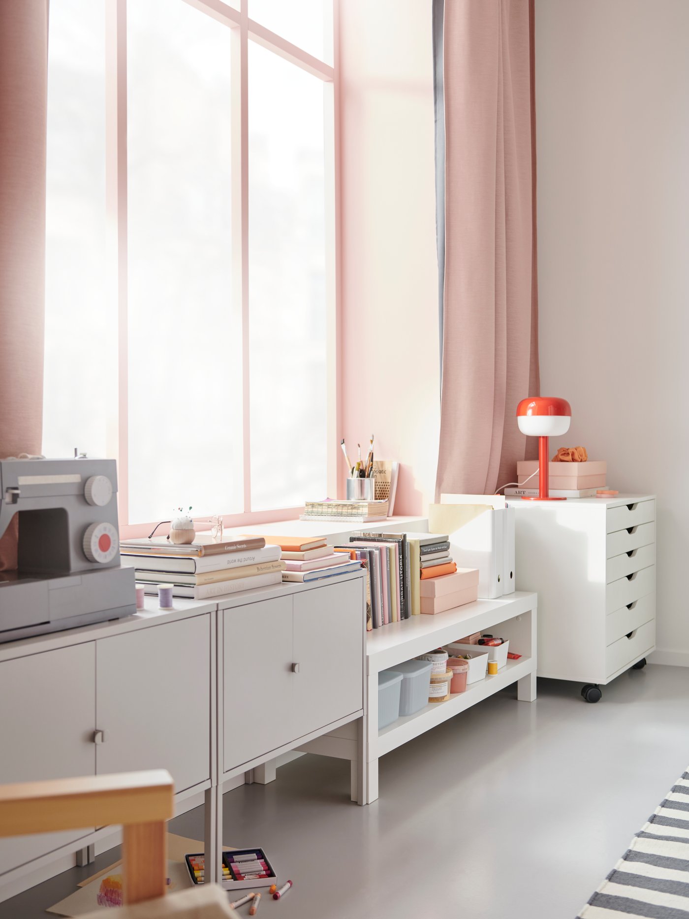 Ett grått LIXHULT, en vit LACK och en ALEX på hjul sida vid sida längs en vägg med fönster.