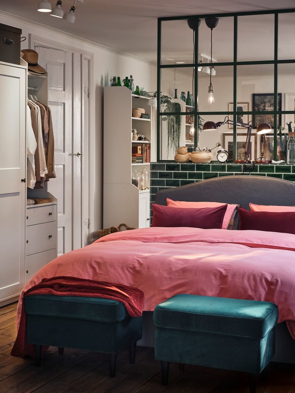 An open-plan space with a HAUGA bed covered in pink bed linen and with two green footstools at the end.