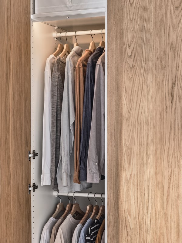A PAX/TONSTAD wardrobe with two doors open showing two KOMPLEMENT hanging rails, one above the other holding various clothes.