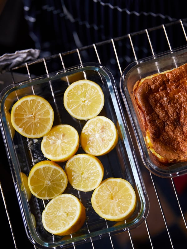 Halved lemons in a glass container beside another glass container with food inside, on top of a cooling rack.