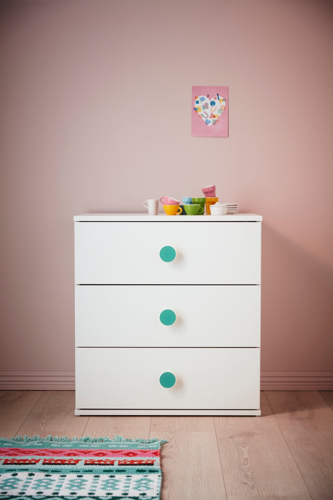 Una cómoda infantil GODISHUS de tres cajones, blanca y con perillas celestes.