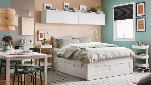 Dormitorio con una estructura de cama tapizada TUFJORD en verde oscuro, 2 lámparas de techo blancas, ropa de cama blanca y una colcha gris.